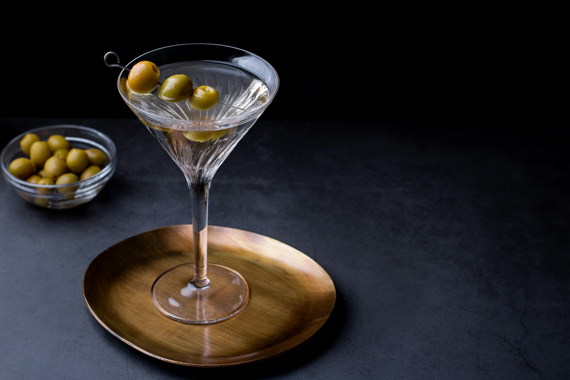 Dirty martini cocktail in martini glass with olives garnish on dark table